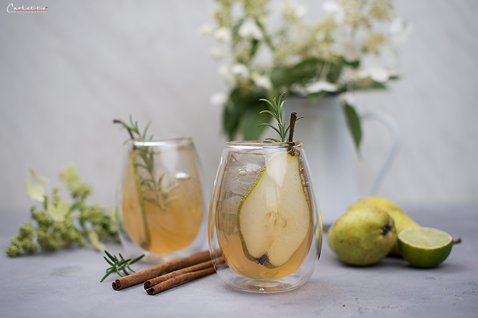 Cocktail mit Birnen und Gin auf grauem Untergrund, Birne, Zimtstange, Blumen in weißer Vase